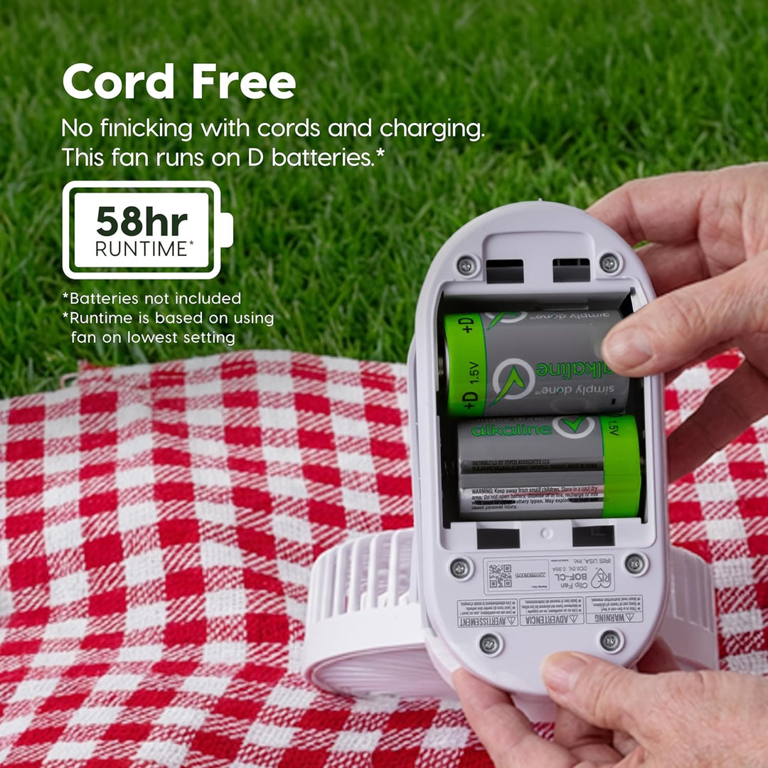Hand holding a battery-operated fan with text highlighting cord-free operation and 58-hour runtime on a grass background.