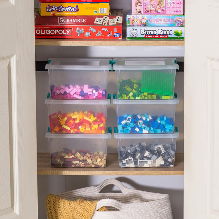 Clear storage bins with colorful toys inside, placed on a shelf with board games above.