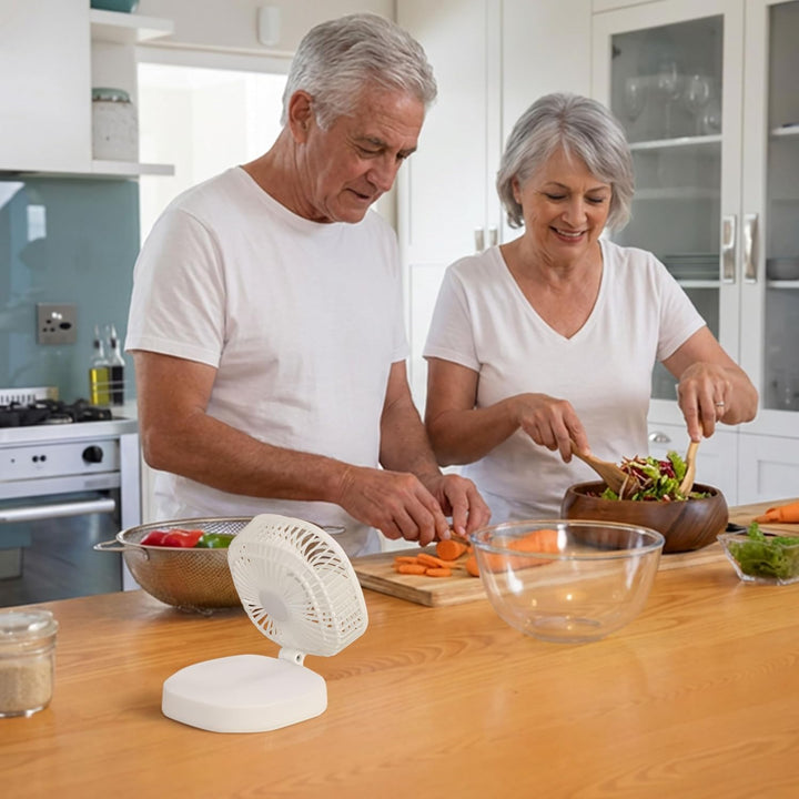 Senior couple preparing food in a kitchen with a small white fan on the counter.