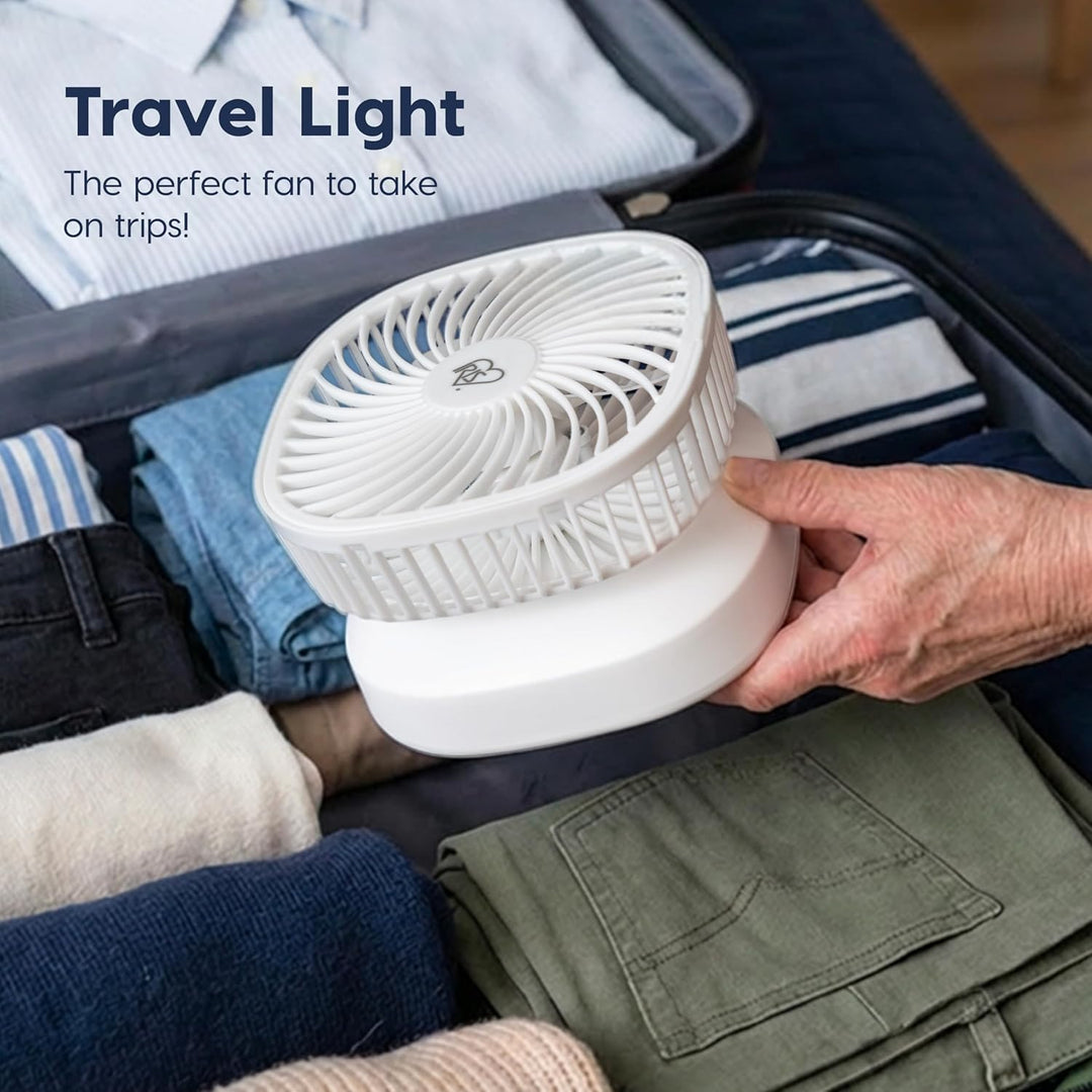 Portable fan being held over a suitcase with clothes, with text 'Travel Light: The perfect fan to take on trips!'.