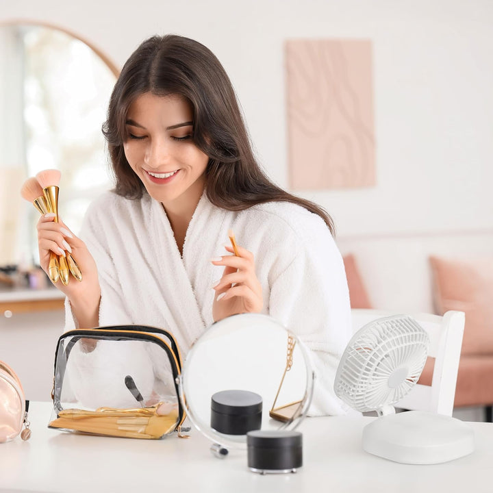Woman in a white robe holding makeup brushes with a table of beauty products in the foreground.