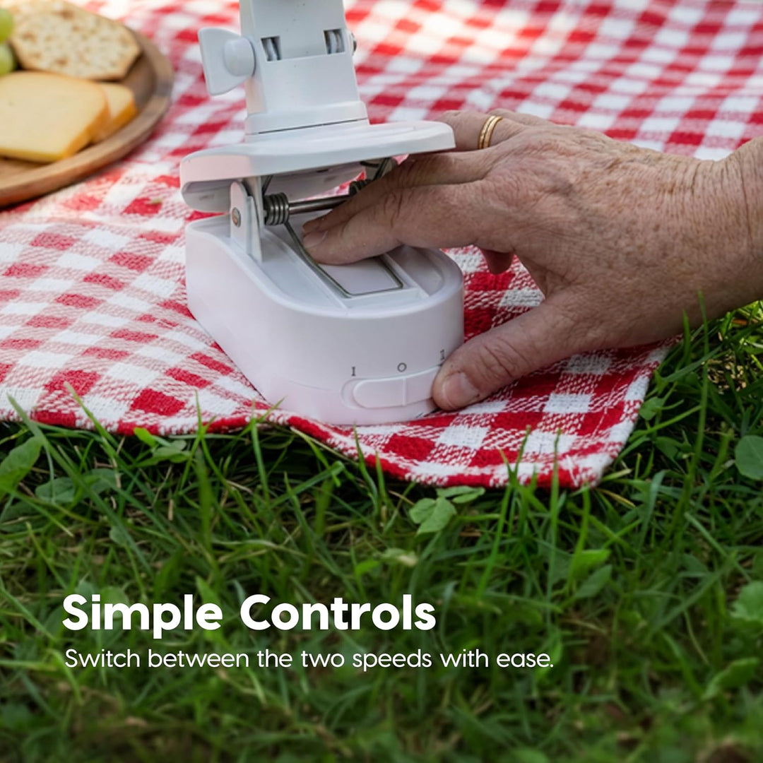 Hand using a kitchen appliance on a red and white checkered blanket outdoors.