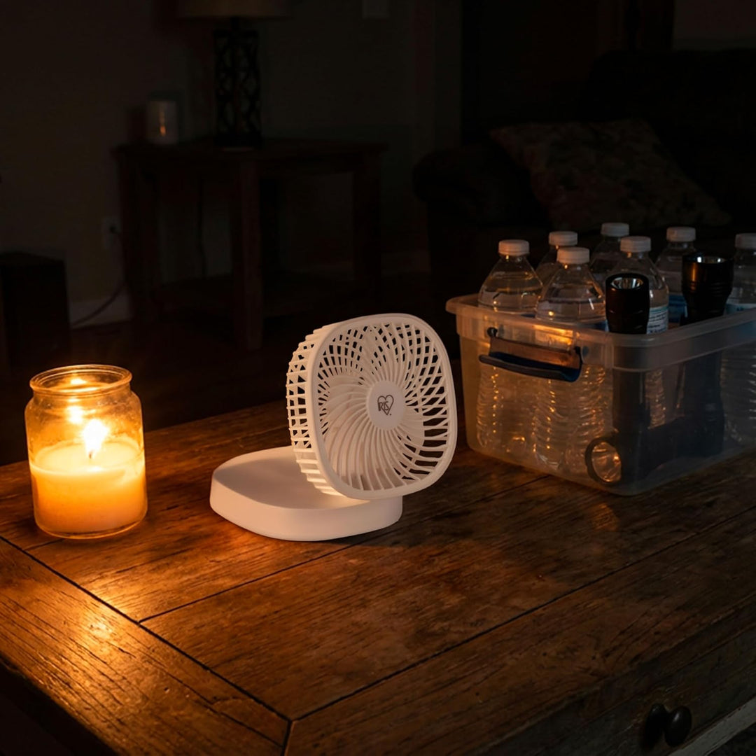 Candle, small fan, and water bottles on a wooden surface in a dimly lit room.