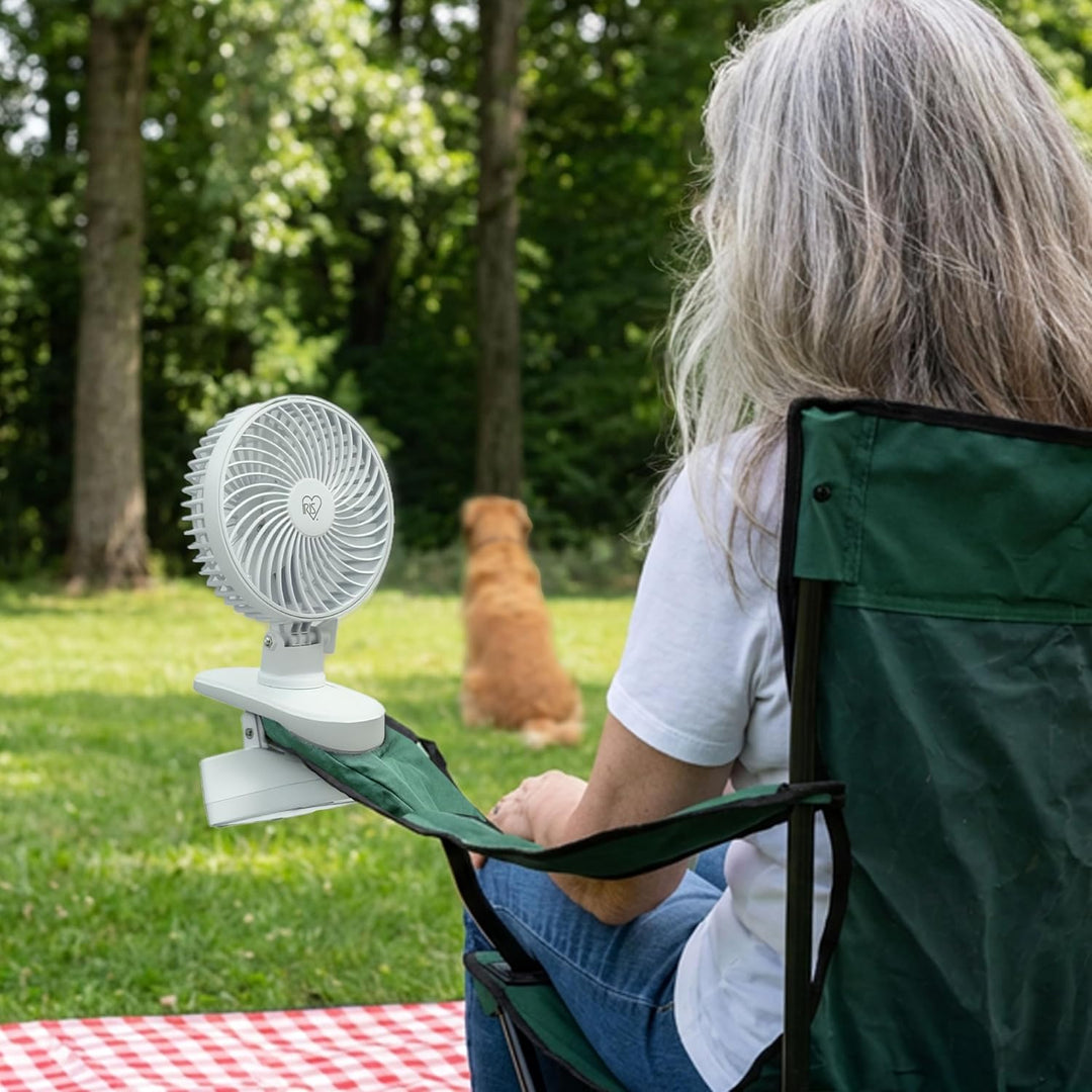 Person sitting outdoors with a portable fan attached to a chair
