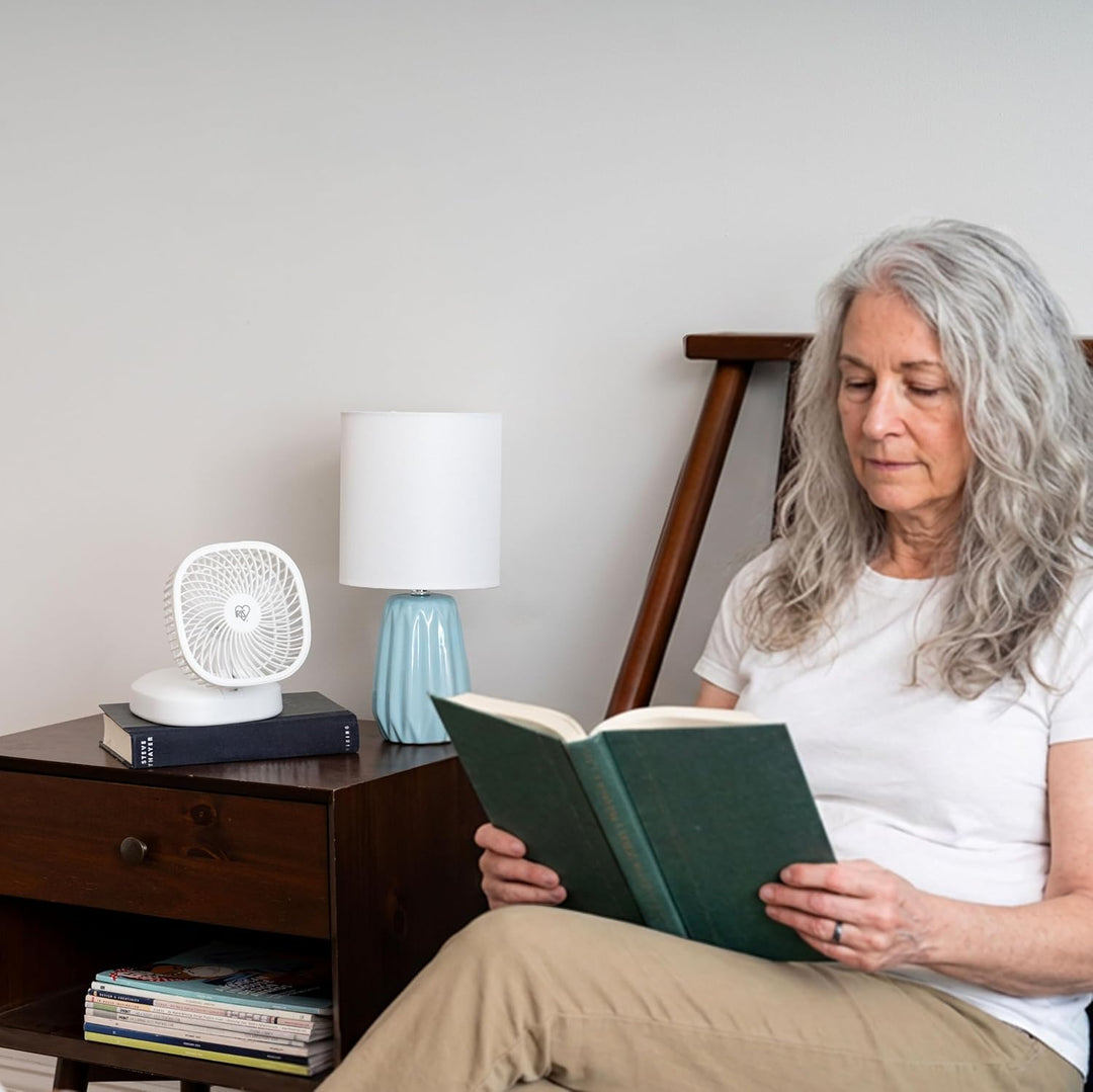 Woman reading a book in a cozy room with a lamp and books on a shelf.